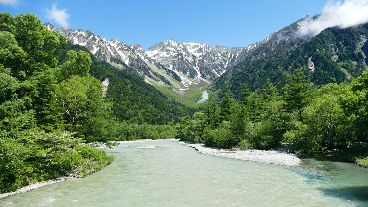 新緑の森を流れる清流と、奥に連なる残雪の山並み