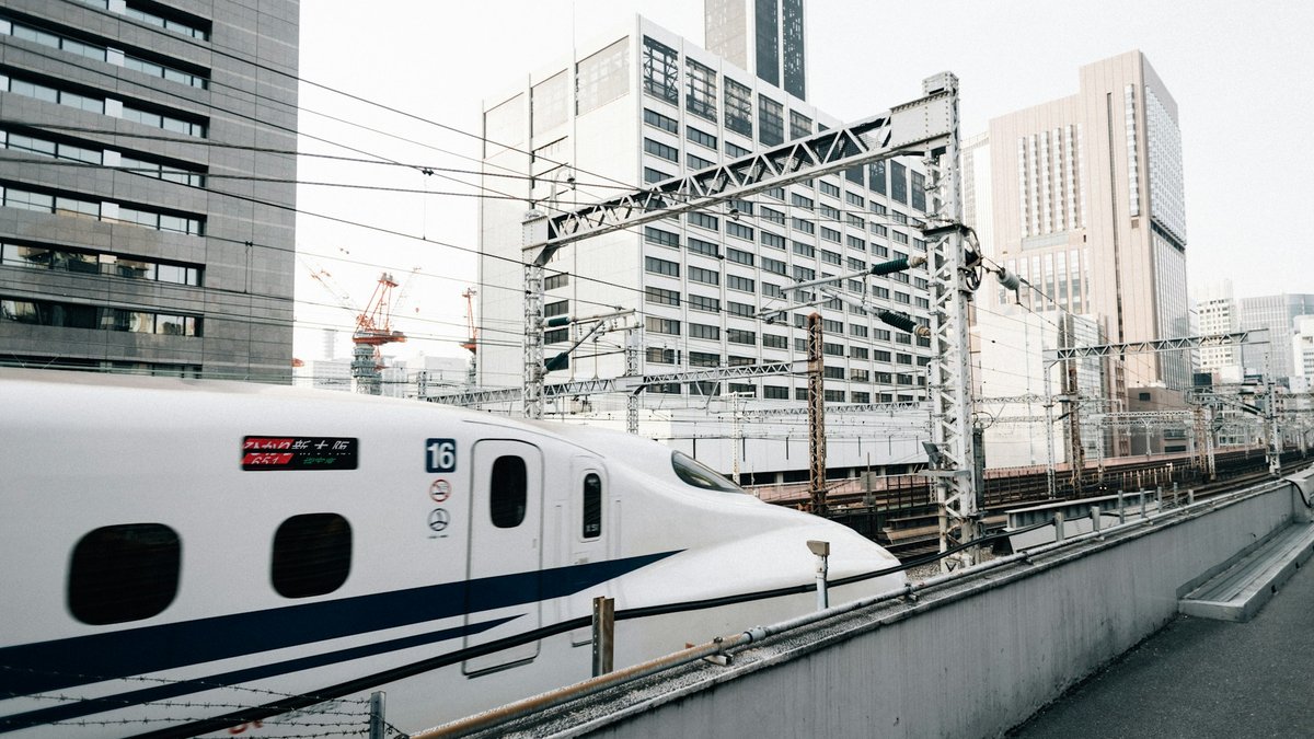 都市のビル群を背に高架を走る新幹線