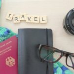 「TRAVEL」と並べた文字ブロックとパスポート、手帳、眼鏡の俯瞰