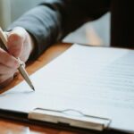 クリップボードに挟んだ書類にペンで記入する手元