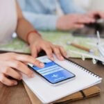 スマートフォンの予約画面を操作する手元。机上に飛行機の模型とカメラ