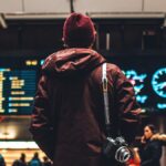 空港の出発案内板を見上げる旅行者。航空券流通の入り口となる運航情報が並ぶ