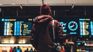 空港の出発案内板を見上げる旅行者。航空券流通の入り口となる運航情報が並ぶ