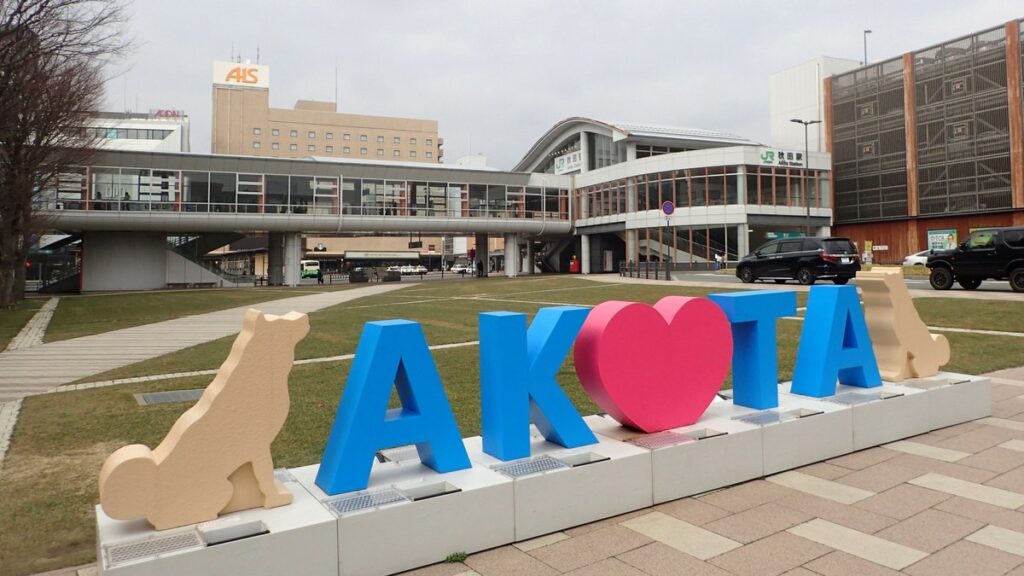 秋田駅前に置かれた「AKITA」の立体文字と秋田犬をかたどったオブジェ。奥にJR秋田駅