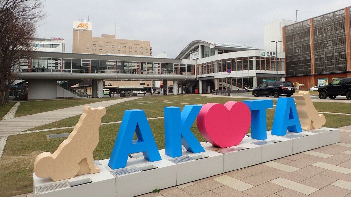 秋田駅前に置かれた「AKITA」の立体文字と秋田犬をかたどったオブジェ。奥にJR秋田駅