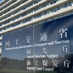 国土交通省の庁舎前に立つ黒御影石の看板。「観光庁」「海上保安庁」の文字が並び、背後に庁舎と青空が広がる