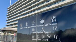 国土交通省の庁舎前に立つ黒御影石の看板。「観光庁」「海上保安庁」の文字が並び、背後に庁舎と青空が広がる