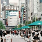 歩行者天国の東京・銀座中央通りを行き交う大勢の人。交差点に「銀座三丁目」の標識が立ち、沿道に百貨店やブランド店のビルが並ぶ