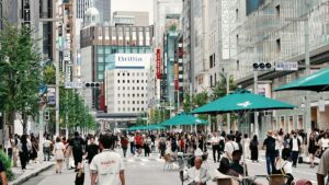 歩行者天国の東京・銀座中央通りを行き交う大勢の人。交差点に「銀座三丁目」の標識が立ち、沿道に百貨店やブランド店のビルが並ぶ