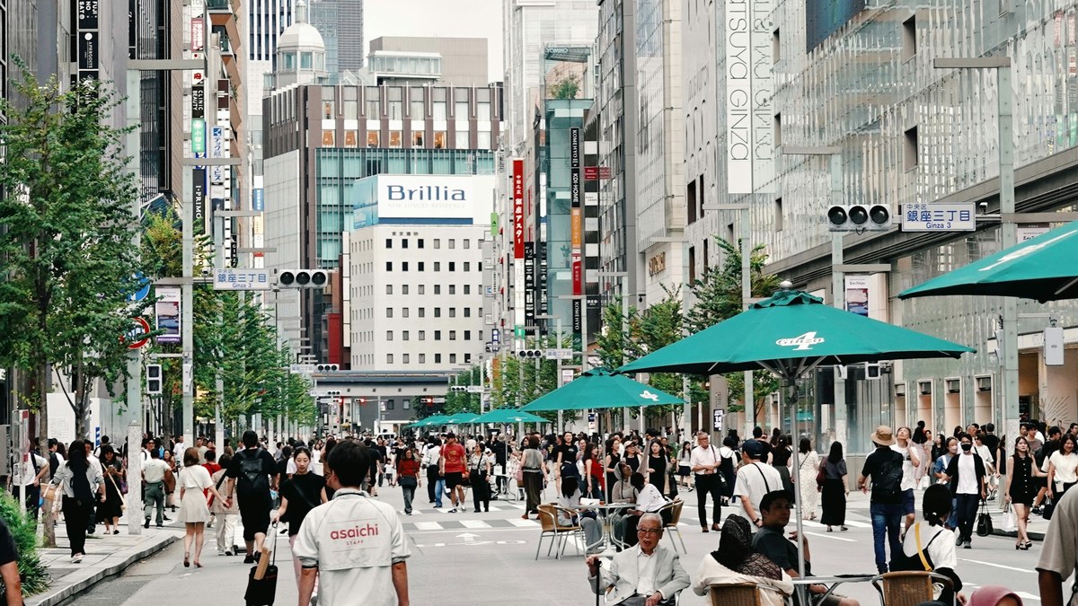 歩行者天国の東京・銀座中央通りを行き交う大勢の人。交差点に「銀座三丁目」の標識が立ち、沿道に百貨店やブランド店のビルが並ぶ