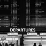 成田空港の出発ロビーに掲げられた大型の出発案内板と、その下を行き交う旅行者