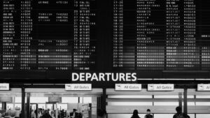 成田空港の出発ロビーに掲げられた大型の出発案内板と、その下を行き交う旅行者