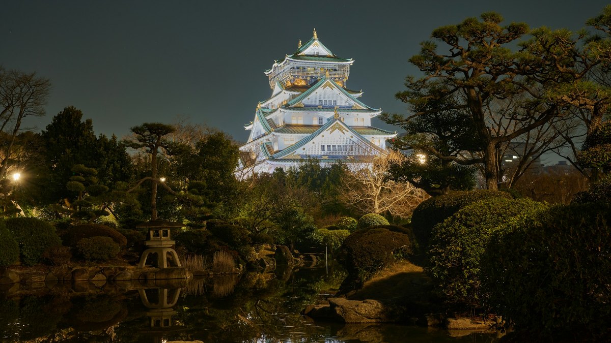 夜間にライトアップされた大阪城天守閣と、手前の日本庭園