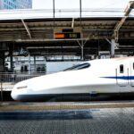新幹線のホームに立つ駅係員と、停車中の白い新幹線。奥の発車案内には新大阪行きが表示されている