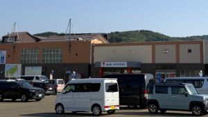 満車に近い駐車場の奥に立つ道の駅の建物。中央の庇に「道の駅 うみてらす名立」の看板が掲げられている