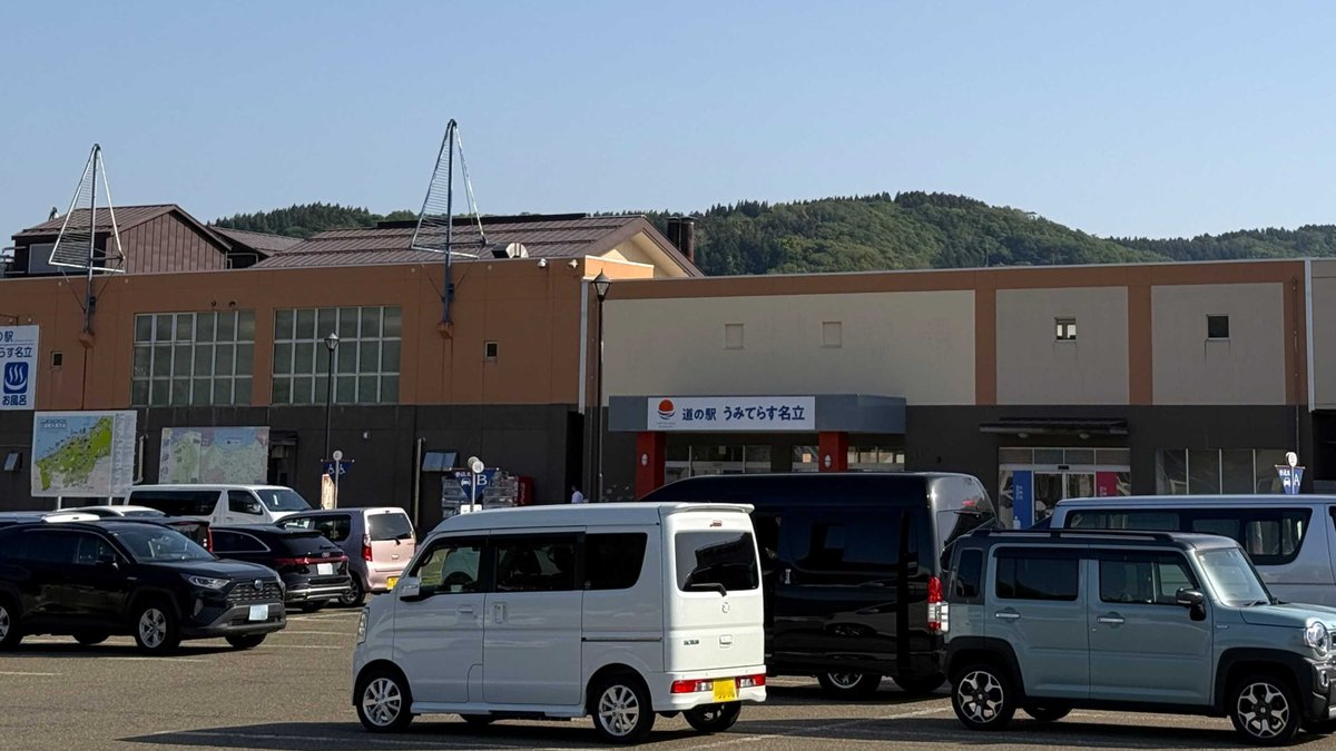 満車に近い駐車場の奥に立つ道の駅の建物。中央の庇に「道の駅 うみてらす名立」の看板が掲げられている