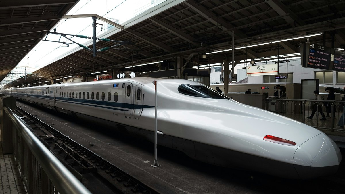 東京駅の東海道新幹線ホームに停車するN700系新幹線と、発車案内表示の下を行き交う乗客