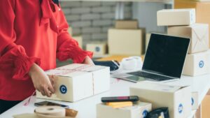 ノートパソコンの横で、海外発送用の段ボール箱を梱包する手元