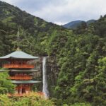 緑の山あいに立つ朱色の三重塔と、その奥に流れ落ちる那智の滝