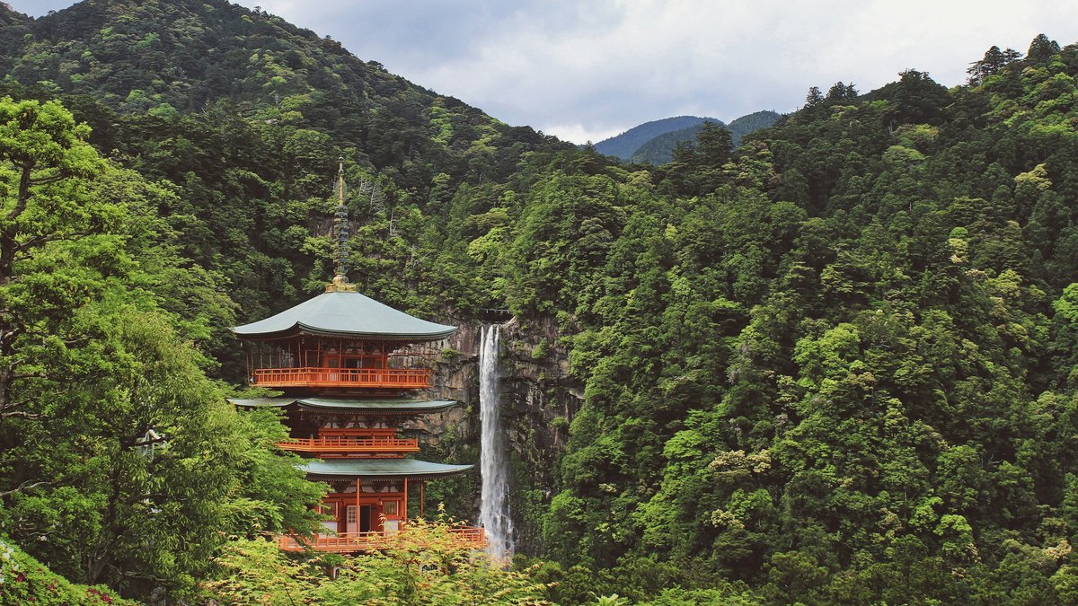 緑の山あいに立つ朱色の三重塔と、その奥に流れ落ちる那智の滝