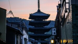 夕暮れの空にそびえる京都・八坂の塔と、手前に並ぶ町家