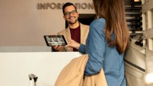 ホテルのインフォメーションカウンターで、スタッフがタブレットの画面を見せながら旅行客に案内している様子