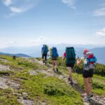 夏の山の稜線の登山道を、大きなザックを背負って一列で歩く登山者のグループ