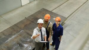 工場の中で設備を指さして説明する作業着の3人