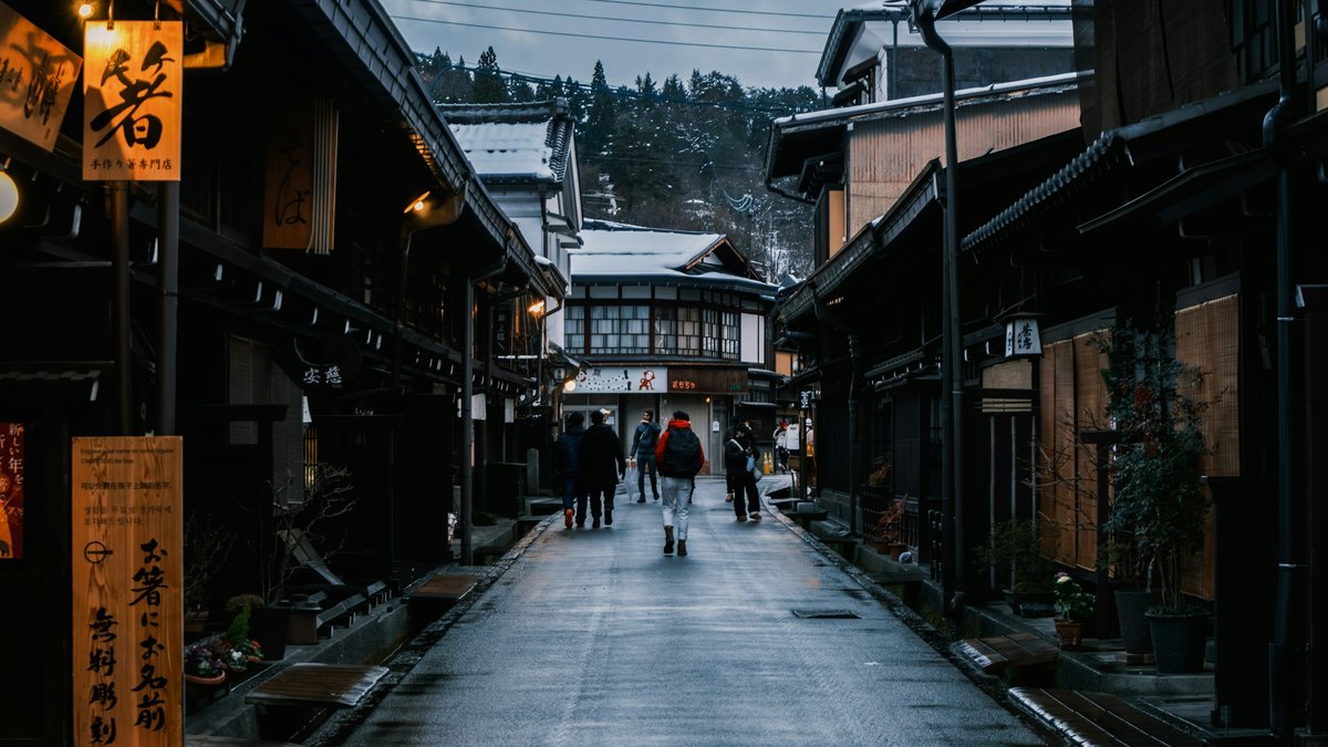 雪の残る山を背に、古い町並みの通りを歩く旅行者たち