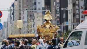 法被姿の町の人たちが、街なかで金色の神輿を担いで進む祭りの様子