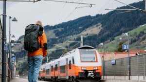 大きなリュックを背負った旅行者が、駅のホームで入ってくる列車を見ている